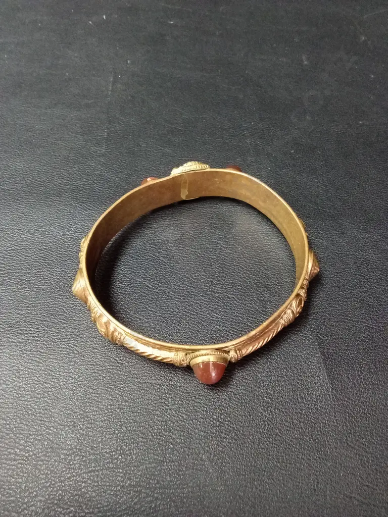 ANTIQUE-STYLE GILT METAL BANGLE WITH CENTRAL LION MASK, FLANKED BY RED GLASS CABOCHONS AND ROPE-TWIST DETAIL Image 1++